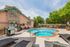 Charming apartment outdoor area with a sparkling round jacuzzi, cozy lounge chairs, barbecue grill, and lush greenery under a bright blue sky.