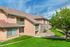 Charming apartment exterior with stone accents, lush landscaping, and inviting balconies under a bright blue sky.