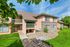 Charming apartment exterior with warm colors, elegant balconies, and lush green landscaping under a vibrant blue sky.