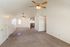 Bright and airy open-plan living area with plush carpet flooring, high vaulted ceilings, and stylish ceiling fans, leading to a cozy kitchen.