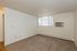 Bright and inviting living space with plush carpeting, large window for natural light, and a wall-mounted air conditioner.