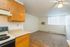 Bright open-plan apartment with a cozy living area featuring carpet flooring, a functional kitchen with wooden cabinets, and ample natural light from a large window.