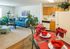 Charming apartment featuring a cozy living area with a plush blue sofa, lush indoor plants, and a stylish kitchen setup. Bright and welcoming dining space with elegant red accents.