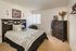 Elegant bedroom with modern dark wood furniture, featuring a cozy bed adorned with stylish linens, alongside a tall dresser topped with vibrant flowers.
