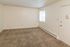 Spacious, sunlit apartment room with plush carpet and large window.