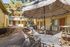 Charming outdoor space with a patio umbrella, cozy seating, and barbecue area amidst lush greenery and a welcoming apartment complex backdrop.