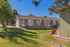 Charming suburban apartment complex featuring well-maintained green lawns, surrounded by mature trees and wooden fencing, under a clear blue sky.