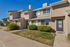 Charming townhouse exterior with clean lines, lush landscaping, and inviting entryway set against a bright, clear sky.