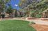 Charming apartment building nestled among lush greenery and mature trees, featuring a well-manicured lawn and beautiful natural landscaping.