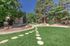 Charming apartment complex surrounded by lush greenery and tall trees, featuring a tranquil pathway leading through a well-maintained lawn.