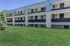 Charming three-story apartment building with blue accents, featuring cozy balconies and surrounded by lush green lawn.