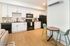 Modern kitchen view with sleek white cabinets, black appliances, and cozy dining space featuring stylish green chairs and a wooden table.