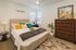 Cozy and modern bedroom featuring a plush bed with colorful pillows, stylish artwork, elegant lighting, and lush indoor plant decor.