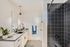 Contemporary bathroom with sleek black-tiled shower, elegant vanity with modern fixtures, and lush green plant accents.