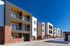 Modern apartment complex with sleek balconies, red brick accents, and a bright blue sky.