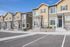 Charming row of modern townhouses with stylish exteriors and neatly landscaped front yards, set against a clear blue sky.