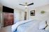 Bright and cozy bedroom featuring a stylish ceiling fan, classic wooden armoire, luxurious bedding, and tasteful wall decor.