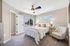 Bright and inviting bedroom with a plush white bed, elegant seating, and modern ceiling fan, complemented by large windows showcasing serene outdoor views.