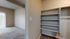 Spacious apartment interior featuring a cozy room with plush carpeting, a bright window with vertical blinds, and ample shelving for storage.
