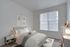 Bright and inviting bedroom with modern decor, featuring a cozy bed with plush pillows, stylish nightstand, and large window with vertical blinds.