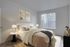 Inviting bedroom with cozy beige bedding, elegant artwork, and abundant natural light from large windows.