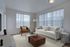 Bright and inviting living room with modern furnishings, featuring a plush white sofa, stylish armchair, decorative coffee table, and large windows allowing natural light.