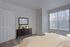 Bright and inviting bedroom with elegant decor, featuring a stylish dresser, large windows with vertical blinds, and a cozy bed with soft linens.