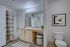 Modern bathroom with stylish vanity mirror and ample lighting, featuring a cozy bathtub and elegant shower curtain, complemented by contemporary art and warm wooden flooring.