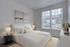Bright and inviting bedroom with a cozy double bed, elegant artwork, and natural light streaming through large windows.