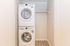 Modern apartment space featuring a sleek, stackable washer and dryer set in a compact laundry closet with wooden flooring.