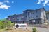 Modern Altitude Apartments building with sleek gray facade and lush green surroundings under a vibrant blue sky.
