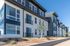 Modern apartment complex with sleek exterior design, large windows, and well-maintained landscaping against a clear blue sky.