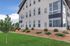 Modern apartment building with large windows, nestled in a beautifully landscaped garden featuring lush greenery and small shrubs.