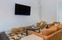 Contemporary living room with cozy brown sofas, stylish woven stools, a sleek black coffee table, and a wall-mounted flat-screen TV.
