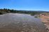 Breathtaking river view under a clear blue sky, surrounded by lush greenery and distant mountains.
