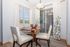 Bright dining area showcasing a round wooden table with elegant white chairs, abundant natural light through large windows, and a tasteful modern chandelier.