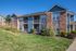 Charming two-story apartment building with a mix of red brick and blue siding, featuring spacious balconies and surrounded by lush greenery under a clear blue sky.