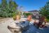 Inviting outdoor patio with cozy fire pit, surrounded by Adirondack chairs, vibrant plants, and a modern grill under a charming pergola.