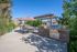 Charming outdoor patio area with a built-in barbecue, shaded pergola, and dining set, surrounded by lush greenery and stylish apartment buildings.