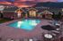Elegant apartment complex with a sparkling pool, surrounded by chic patio furniture, set against a breathtaking mountain sunset view.
