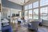 Bright and airy living room with large windows overlooking a sparkling pool, featuring chic seating, a modern chandelier, and a stylish kitchen bar area.