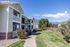 Charming two-story apartment complex with private balconies, nestled against a scenic mountain backdrop and bordered by lush greenery.