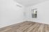 Modern, sunlit room featuring pristine white walls, elegant wood flooring, and a large window for natural light.