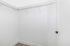 Spacious walk-in closet with sleek white walls, modern black door handle, and ample hanging space for storage.