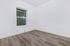 Bright and airy room featuring elegant wood flooring, large window with lush greenery view, and clean white walls.