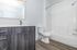 Modern bathroom with sleek gray cabinetry, elegant countertop, and spacious bathtub, highlighted by contemporary fixtures and natural wood flooring.