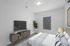 Modern bedroom featuring a sleek TV stand, cozy bed with stylish linens, and a lush green plant by the window, offering a serene and inviting ambiance.