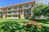 Charming apartment complex with a sunny three-story facade, surrounded by lush green grass, featuring outdoor picnic seating for relaxation and gatherings.