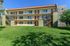 Charming three-story apartment building surrounded by lush green lawn, featuring modern exterior with balconies and staircases.