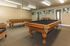 Elegant recreation room with a luxurious wooden billiards table, mirrored wall, and cozy seating area, perfect for entertainment.